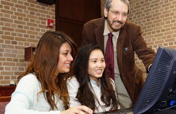 Two female students at computer with business professor Dr. Hassan Shirvani at the University of St. Thomas - Houston