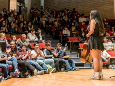 Student holding guitar on stage as part of Celts Got Talent competition in Jones Hall on the campus of the University of St. Thomas in Houston, Texas