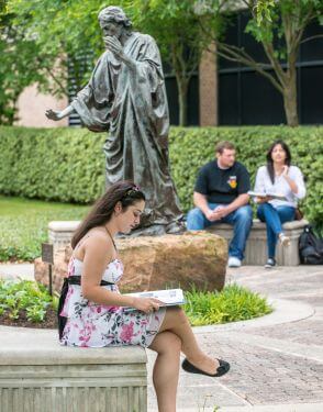 Psychology major studies in front of Jesus sculpture on University of St. Thomas - Houston campus