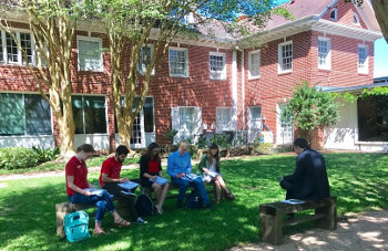 Students sit with professor outside University of St. Thomas - Houston Honors Program House