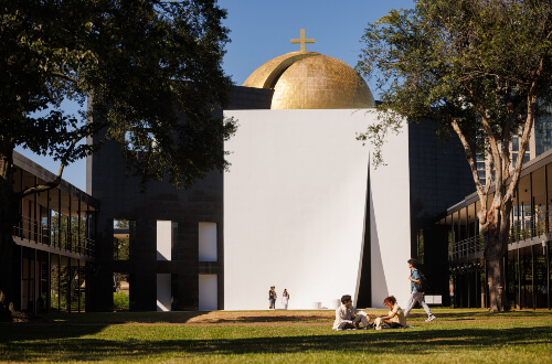 Undergraduate students talking in front of Chapel of St. Basil at the University of St. Thomas in Houston, Texas